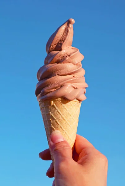 Mouthwatering Chocolate Soft Serve Ice Cream Cone in Hand Against Blue Sunny Sky