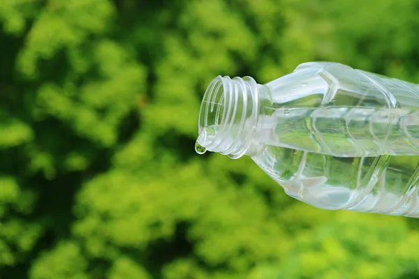 Closeup of drinking water dropping from PET bottle with blurry green foliage in the backdrop