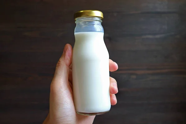 Glass bottle of milk in hand against black wooden wall