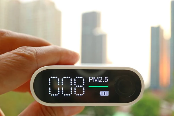 Closeup of an air quality sensor in hand against group of high buildings