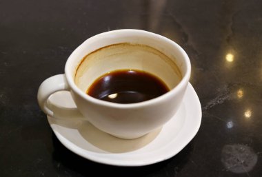 Yarım fincan sıcak kahve, siyah masaya izole edilmiş.