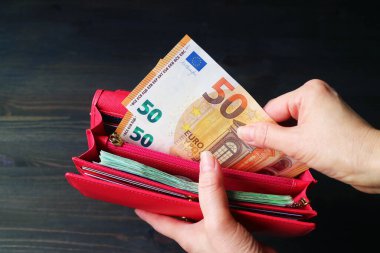 Kırmızı bir cüzdanda bir avuç Euro banknotunu tutan bir kadının resmi.
