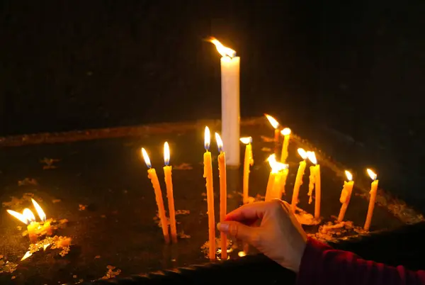 Woman\'s Hand Placing Lit Candle into the Votive Candle Stand inside the Church