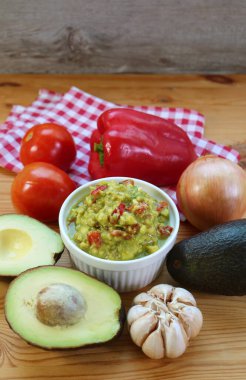 Taze avokado ve diğer malzemelerle çevrili bir kase taze Guacamole.