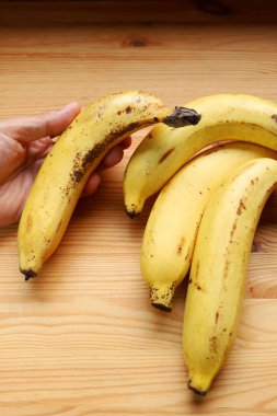 Hand holding a ripe banana with brown spots on its peels clipart