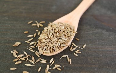 Tahta kaşıkta kurutulmuş kimyon tohumu ve biraz da masaya serpiştirilmiş.