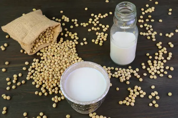 stock image Cup of Soy Milk with a Bottle and Burlap Bag of Soybeans on Black Wooden Table