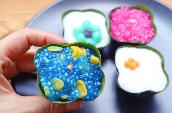 stock image Hand Picking Thai Dessert of Two Layered Coconut Milk Pudding Called Khanom Tako in Upside-down Version with Traditional Versions in a Plate