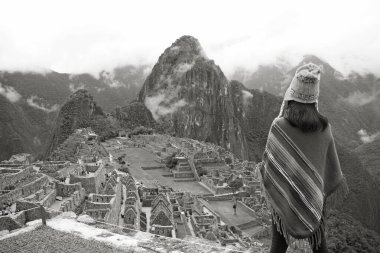 Monochrome Image of a Woman in Poncho Looking at the spectacular ancient Inca ruins of Machu Picchu citadel, Cusco, Peru, South America clipart