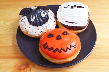 Tahta arka planda izole edilmiş üç farklı Cadılar Bayramı Hayalet Donutu plakası.