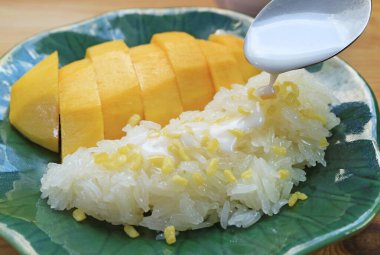 Çiğnenmiş Yapışkan Pirinç üzerine kremalı hindistan cevizi sütü ekliyorum. Sulu taze mangoyla servis ediliyor.