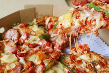 Karton kutudan çıkarılan esnetilmiş peynirli bir dilim pizzanın yakın çekimi.