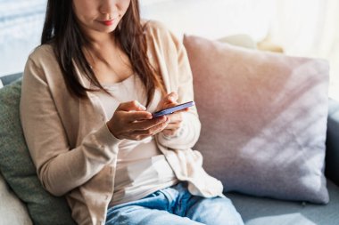 Genç bir kadın akıllı telefon kullanıyor ve sabahları evdeki kanepede dinleniyor.