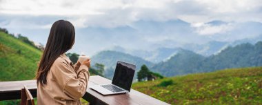 Young woman freelancer traveler working online using laptop and enjoying the beautiful nature landscape with mountain view
