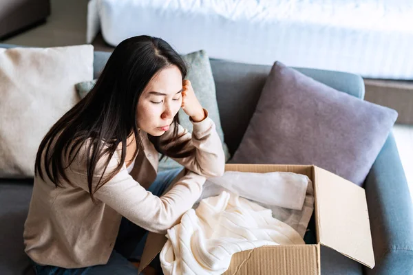Dissatisfied young woman unpacking parcel at home received damaged and wrong online shopping order