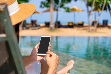Yaz tatili için seyahat ederken dinlenen ve havuz başında cep telefonu kullanan genç bir kadın gezgin.