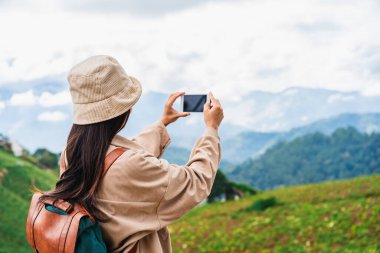 Genç bir kadın gezgin akıllı telefonuyla fotoğraf çekiyor. Sis denizinde ve dağda gün doğumunda.