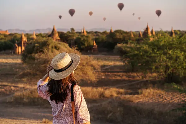Genç kadın gezgin balonlarla Bagan, Myanmar 'daki antik tapınağın üzerinde gün doğumunda eğleniyor.