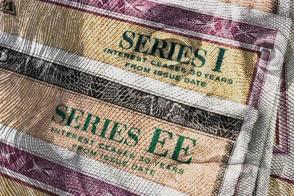 Series I and Series EE US Savings Bonds with 100 dollar bill overlay. Savings bonds are debt securities issued by the US.