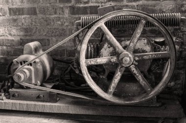 Sepya tonunda antika hava kompresörü. Arka planda bobin olan ilginç bir tekerlek tasarımı.