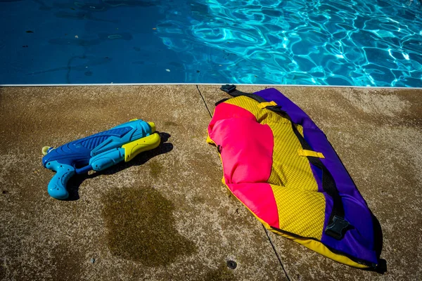 Colourful safety life jacket and water gun on concrete patio facing pool