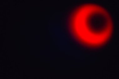 Parlak kırmızı bulanık ışığın eliptik şekli ve siyah bir arkaplanda karanlık bir delik.