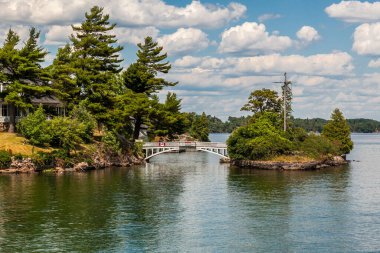 A view in Ontario, Canada of the Thousand Islands with cottage on the river, bridge and the surrounding nature on a summer afternoon clipart