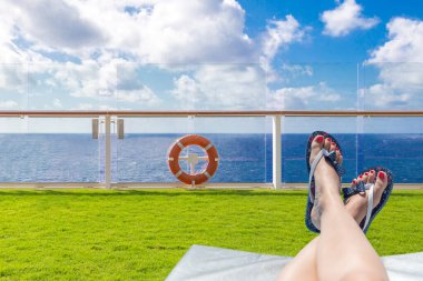 Female feet on a sunbed on a deck of cruise ship with ocean on background with blue sky
