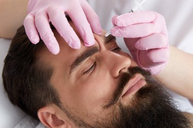 Closeup of bearded man getting beauty injection at aesthetic clinic. Doctor injecting anti-aging filler in handsome male face. Male cosmetology, aesthetic medicine concept