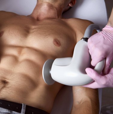 Man receiving fat reductive skin lifting body treatment on modern equipment at cosmetology clinic, male body care concept