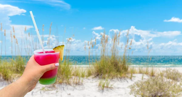 Hand holding a glass with cocktail and straw, Sand Dunes with Grass on Beach