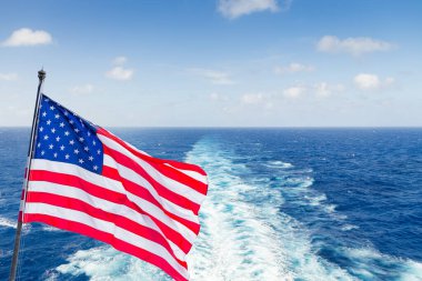 USA national flag on cruise ship with wake or trail on ocean surface on background