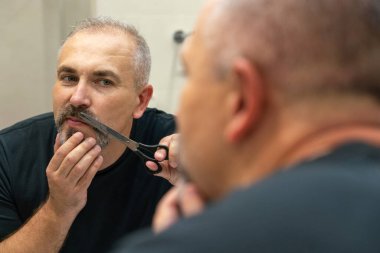 Portrait of Middle-aged handsome man cutting his beard with scissors