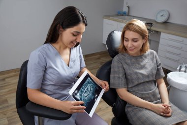 Doktor dişçi hastaların dişlerini röntgende gösteriyor.