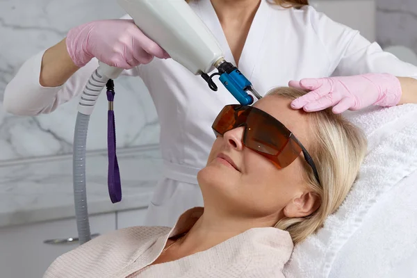 Woman receiving a laser treatment in cosmetology clinic wearing glasses