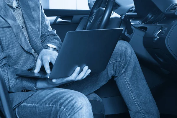 Professional man with a laptop in car tunes tuning control system, updating software, gaining access through to computer, sitting in cabin