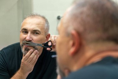 Portrait of Middle-aged handsome man cutting his beard with scissors