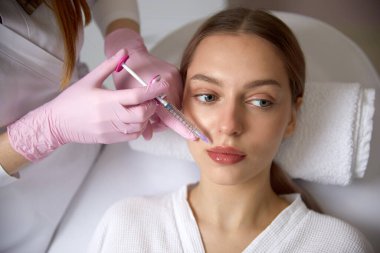 Rejuvenating facial injections procedure for tightening and smoothing wrinkles on the face skin of a beautiful, young woman in a beauty salon
