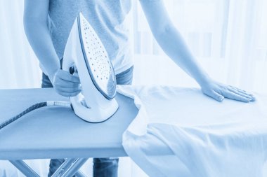 Ütü masasındaki beyaz gömleği ütüleyen kadın ellerini kapat.