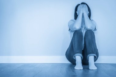 Üzgün kadın boş bir odada yerde yalnız başına, umutsuzluk ve yalnızlık içinde.