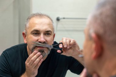Portrait of Middle-aged handsome man cutting his beard with scissors