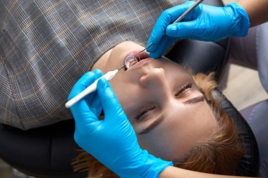 Dentist checking teeth of a patient with dental mirror. Woman having teeth examined at dentists