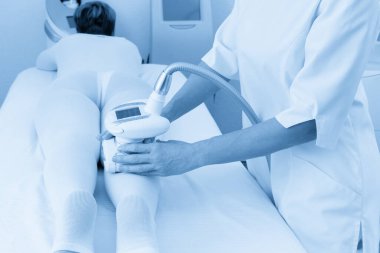 Beyaz takım elbiseli bir kadın spa salonunda selülit karşıtı masaj yaptırıyor. Klinikte LPG ve vücut şekillendirme tedavisi