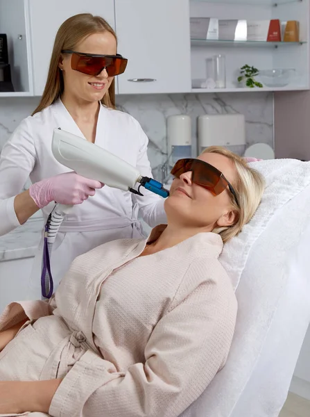 Woman receiving a laser treatment in cosmetology clinic wearing glasses