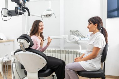 Female dentist talking to a patient during appointment in modern dental clinic before teeth treatment