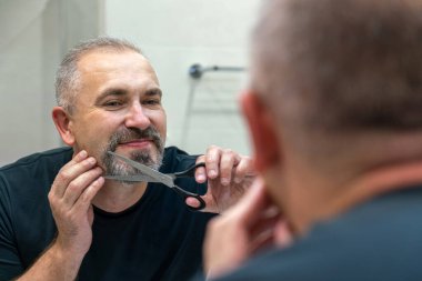 Portrait of Middle-aged handsome man cutting his beard with scissors