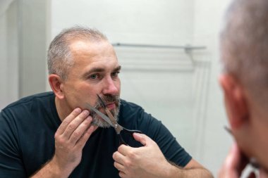 Portrait of Middle-aged handsome man cutting his beard with scissors