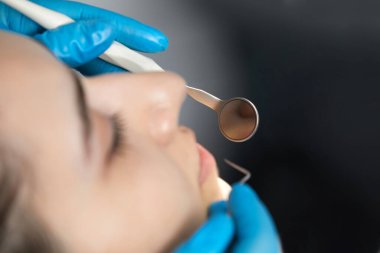 Dentist checking teeth of a patient with dental mirror. Woman having teeth examined at dentists
