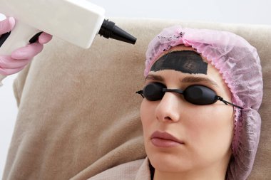 Carbon peeling in beauty salon. Cosmetologist applying black mask on the face of beautiful woman for carbon peeling