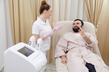 Güzellik uzmanı kozmetoloji dolabında genç bir adamla konuşuyor.